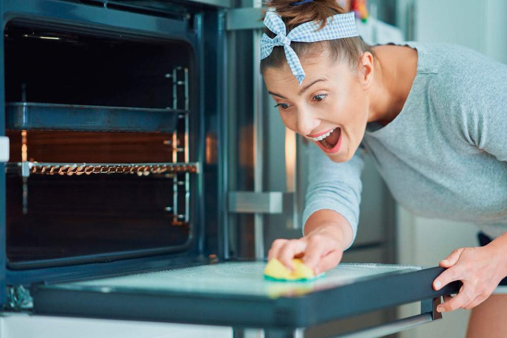 Mujer feliz muestra cómo limpiar un horno muy sucio